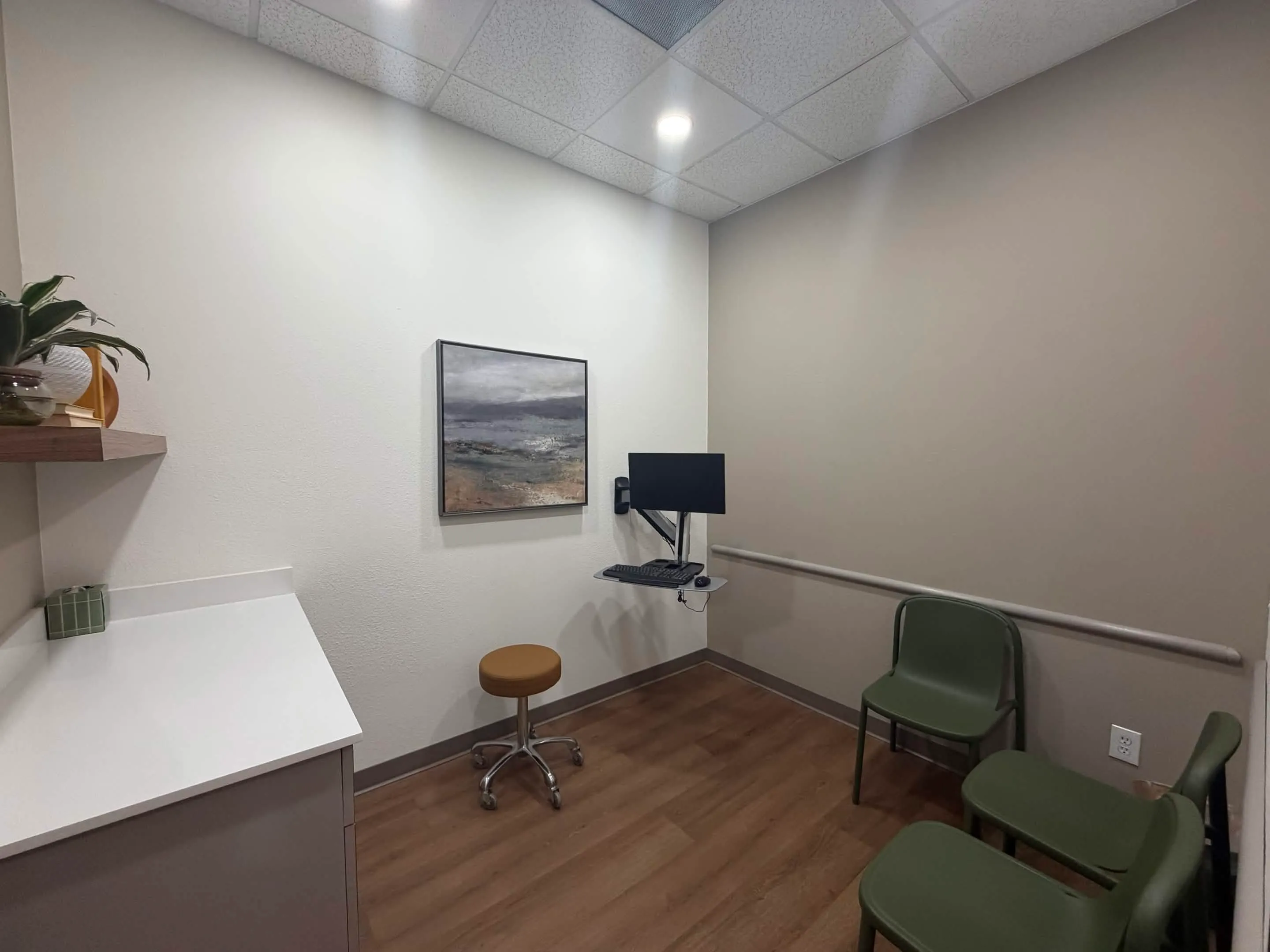 Private patient room with green chairs, artwork, and a consultation workstation